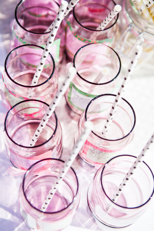 Closeup of decorative pink colored party glasses with straws on table outdoors on bright dayの写真素材