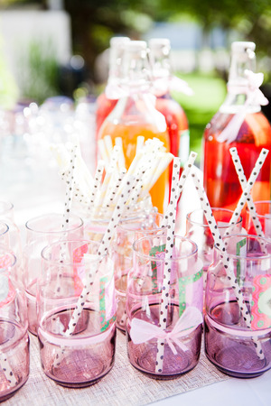 Closeup of decorative pink colored party glasses with straws on table outdoors with bottle of fruit juice in backgroundの写真素材