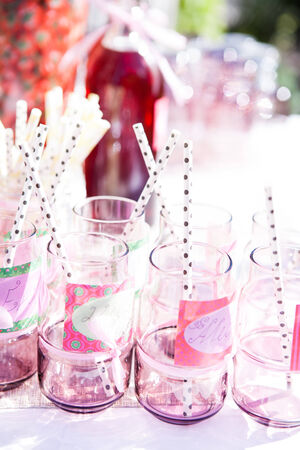 Closeup of decorative pink colored party glasses with straws on table outdoors with bottle of fruit juice in backgroundの写真素材