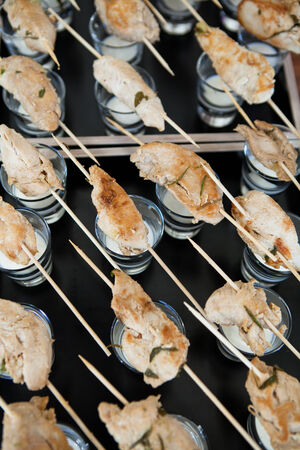 Closeup of rows of cooked chicken appetizers on wooden skewers resting on glasses with mayonnaise sauce dip ready for servingの写真素材