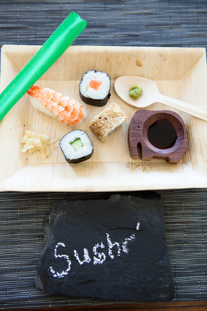 Closeup of plate of sushi with soy sauce and hot wasabi paste and fresh ginger and decorative stone label with textの写真素材