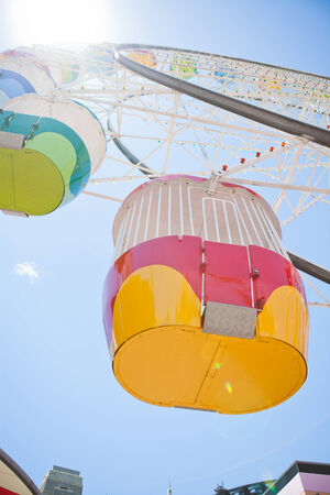 Upward view to colorful ferris wheel and carriages at amusement park on sunny summer dayの写真素材