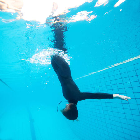 Female diver calmly diving downwards through surface into swimming poolの写真素材