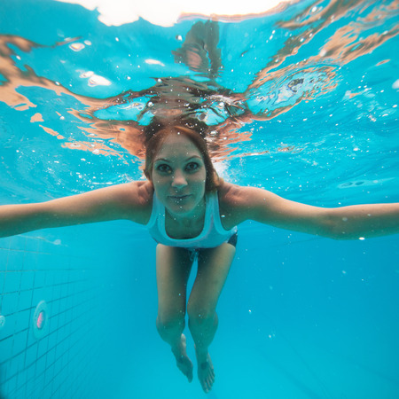 Attractive female with eyes open looking and smiling while underwater in swimming poolの写真素材