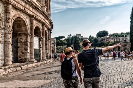 a couple of tourists visit the Coliseum, both with his hat, he points to the right, a lot of tourists in the background, clear sky and coliseum on the leftの写真素材