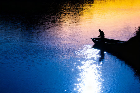Silhouette of a fisherman in a boat on the lake at sunsetの素材