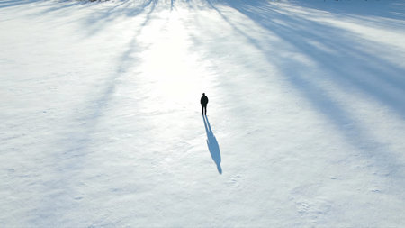 Silhouette of a man walking in the snow on a sunny dayの素材