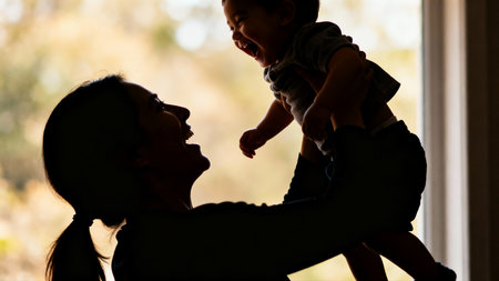 Silhouette of happy mother and her little daughter playing together at homeの素材