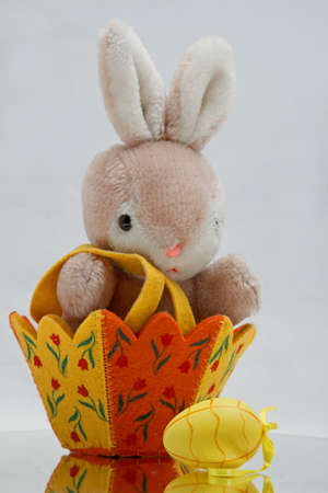 A plush toy bunny sitting in an Easter basket with yellow Easter eggの写真素材