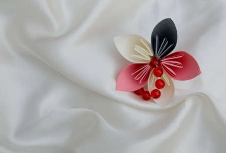 Beautiful colourful folded origami flower on a white shiny textile backgroundの写真素材