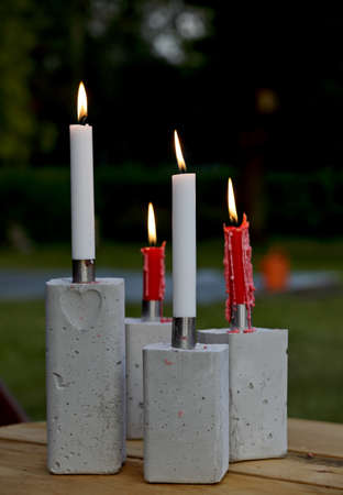 Red and white candles burning on a table outdoors. Candlesticks are self made of concrete and steel.の写真素材