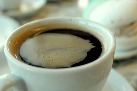 Black coffee with foam to drink in a porcelain cup standing on the table on the background of sweet...