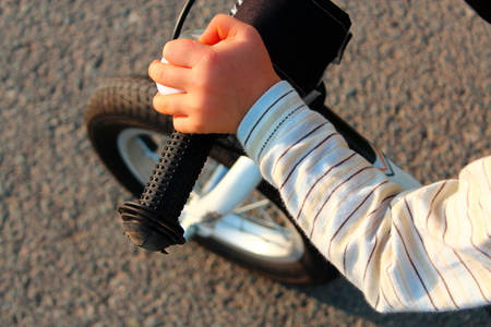 Children's hand on the steering wheel of a bicycle riding along an asphalt road.の写真素材
