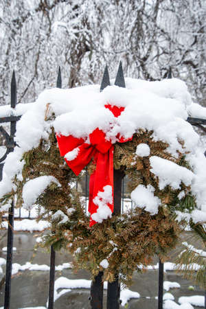 Christmas wreath with red ribbon on a metal fence covered with snowの写真素材