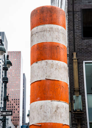 A vertical shot of an orange and white striped pole in the cityの写真素材