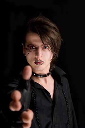Gothic boy with artistic make-up pointing his hand as a gun, isolated on black background の写真素材