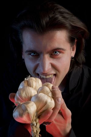Vampire with scary eyes is licking garlic, red horror light, isolated on black background の写真素材