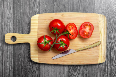 Top view of fresh tomatoes and knife on chopping board on gray table の写真素材