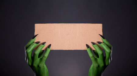 Green monster hands with black nails holding empty piece of cardboard, Halloween themeの写真素材