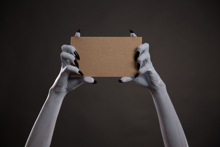 Creepy white hands with black nails holding blank cardboard, Halloween themeの写真素材