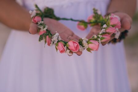Bride's hands with a wreath of small roses.