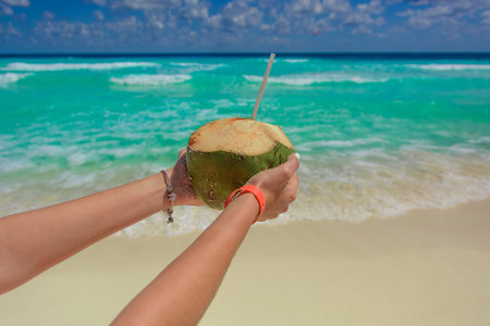 Coconut with a straw in female hands on the background of the seaの写真素材