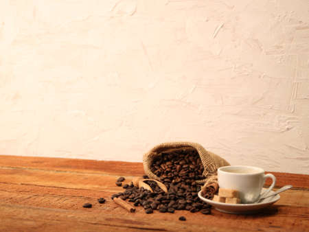 Cup of coffee with coffee beans, burlap sack, bag, cinnamon sticks and scoop on old wood tableの写真素材