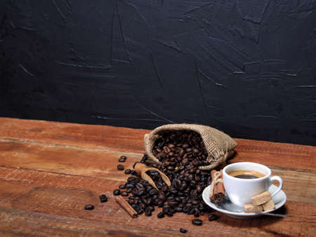 Cup of coffee with coffee beans, burlap sack, bag, cinnamon sticks and scoop on old wood tableの写真素材