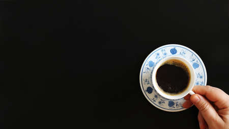 Male hand holding a coffee cup. Close up of a hand of man holding a warm mug with fresh coffee. Coffee concept isolated on black backgroundの写真素材