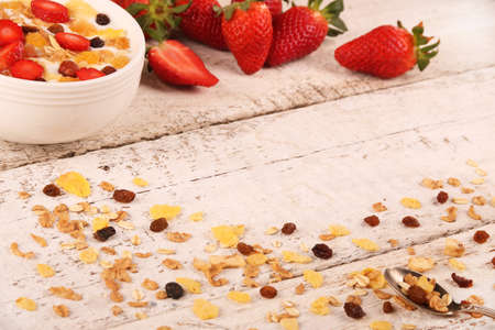 Bowl of yogurt with strawberries and granola muesli, over a white rustic wood background.