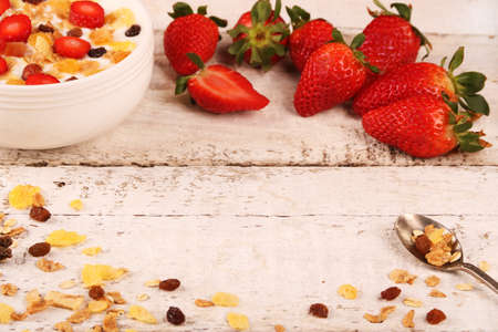 Bowl of yogurt with strawberries and granola muesli, over a white rustic wood background.