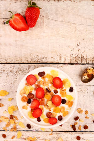 Bowl of yogurt with strawberries and granola muesli, over a white rustic wood background.