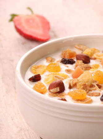 Bowl of yogurt with strawberries and granola muesli, over a white rustic wood background.