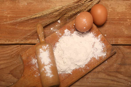 Kitchen rolling pin, wooden board with flour on rustic wooden background ears and eggs for making...