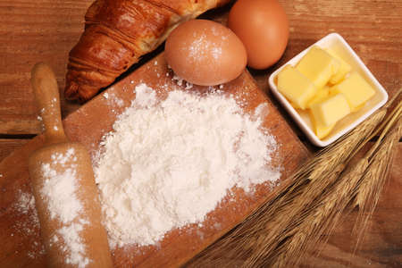 Kitchen rolling pin, wooden bowl with flour on rustic wooden background and butter for making croissant on table.の写真素材