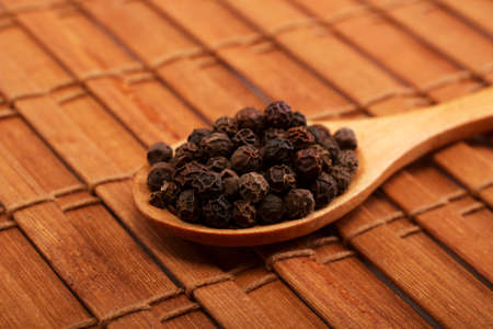 Wooden serving spoon full of black pepper spice over the wooden background