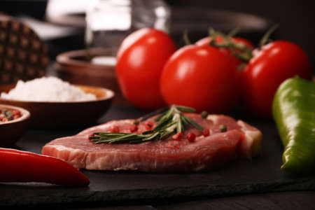 Raw pork meat steak with vegetables, peppers, tomato, salt, rosemary and spices cooking over stone cutting table. Top view.の写真素材