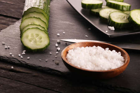 Fresh sliced green cucumbers with knife and salt on black plate and black wood rustic table.の写真素材