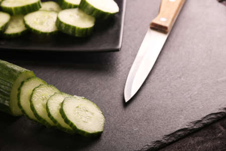 Fresh sliced green cucumbers with knife on black plate and black wood rustic table.の写真素材