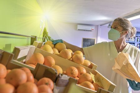Woman buying fruits and vegetables direct from producer during confinement and wearing her protective mask in the shopの写真素材