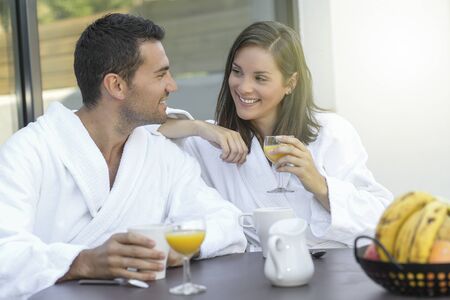 Happy young couple in bathrobes having breakfast outdoorsの写真素材