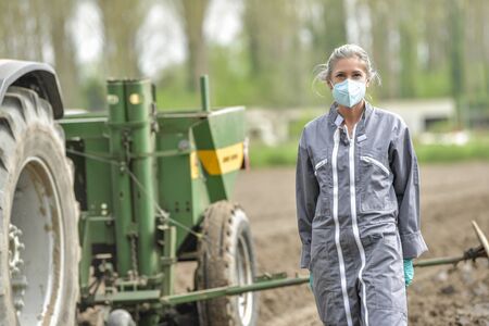 Portrait of a woman  farmer wearing her protective mask in the field beside a tractorの写真素材