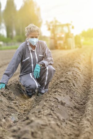 Female farmer  analyses the soil before planting and wearing a protective mask against coronavirusの写真素材