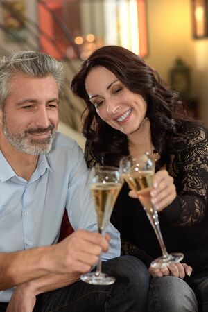Happy elegant middle-age couple celebrating something with champagne at homeの写真素材