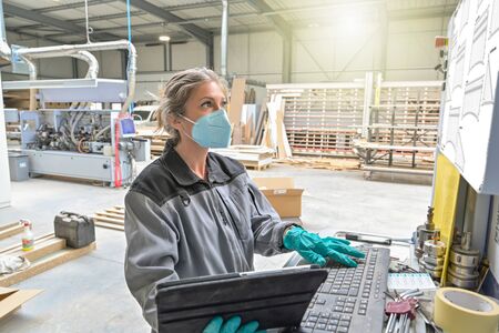 Woman engineer operating on a industrial digital machine and wearing protective mask against coronavirusの写真素材