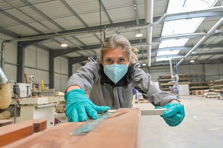 Woman worker operating in the carpentry workshop  and wearing protections againt covid-19の写真素材
