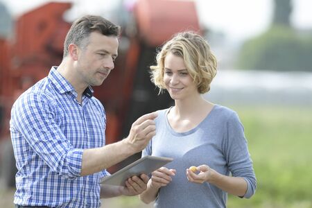 Couple of Farmer analyses the potatoes harvesting data next to the tractor in a fieldの写真素材