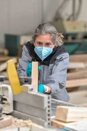 Woman worker operating on a woodworking machinery and wearing protections againt covid-19の写真素材