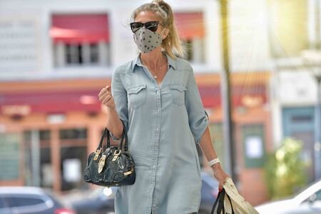 Attractive middle age urban woman walking in the street  and carrying bags for shopping while she is wearing a protective mask against corona virus.の写真素材