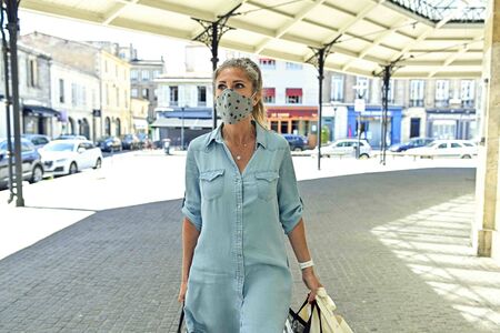 Urban woman doing shopping while she is wearing a protective mask in the street against covid-19の写真素材